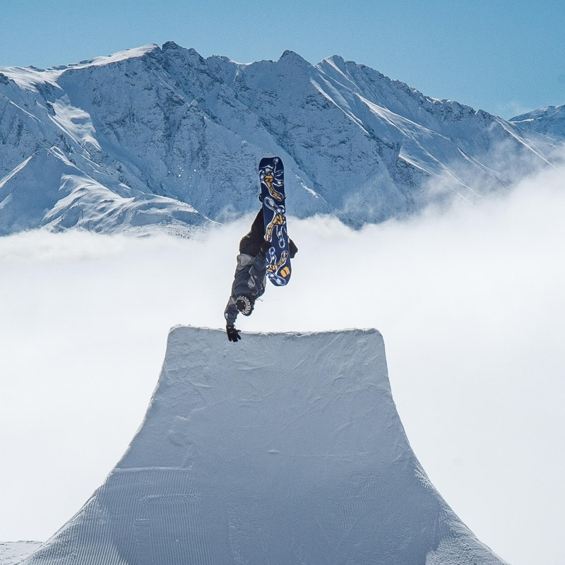 Armada Snowboards Sicko with rider doing lip grab on jump with mountain background