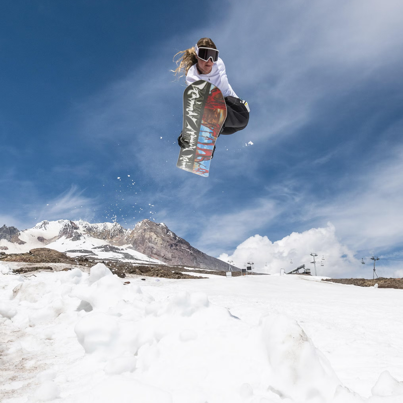 Armada Snowboards Squonk with rider in air leaving jump with patchy snowy mountain behind