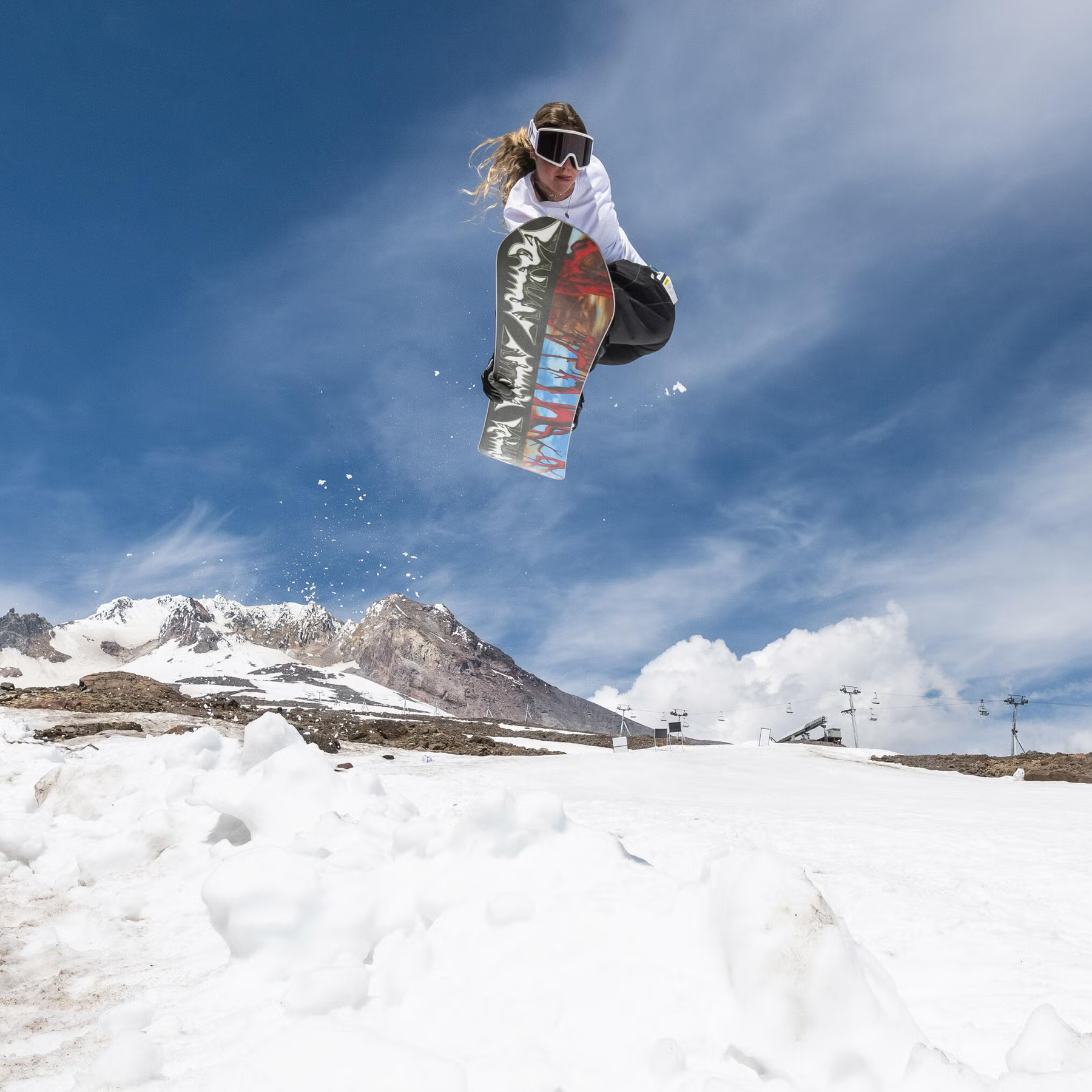 Armada Snowboards Squonk with rider in air leaving jump with patchy snowy mountain behind