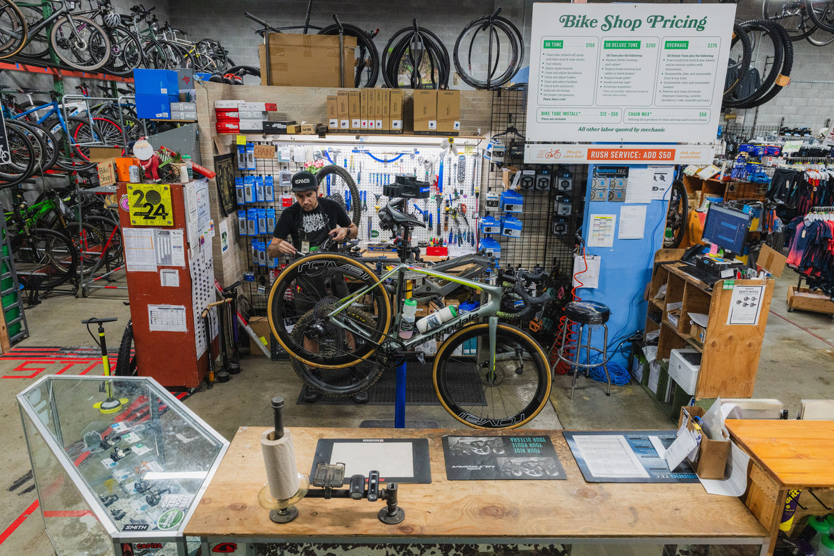 Bicycle repair shop with a mechanic working on a bike, various tools, and equipment.