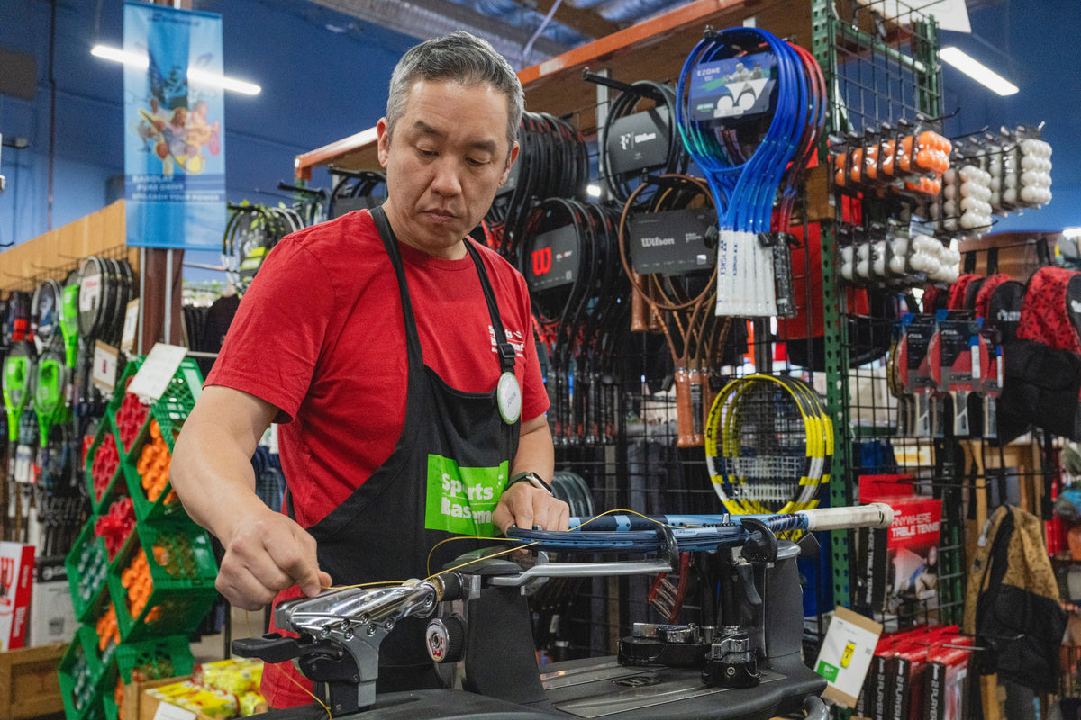 Man in a red shirt and apron working with sports equipment in a store.